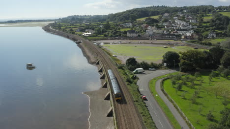 Aerial-shot-of-drone-following-a-train-along-the-Devon-coast-at-the-river-Exe's-mouth-and-the-train-disappearing-into-the-distance,-located-near-Starcross-station
