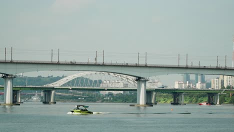 Speed-boat-and-Water-Rescue-Unit-Motorboat-Moves-with-Speed-at-Han-river,-Traffic-on-Yanghwa-Bridge-and-Dangsan-Railroad-Bridge-in-the-foreground,-Seoul-Marina-club-on-sunny-day