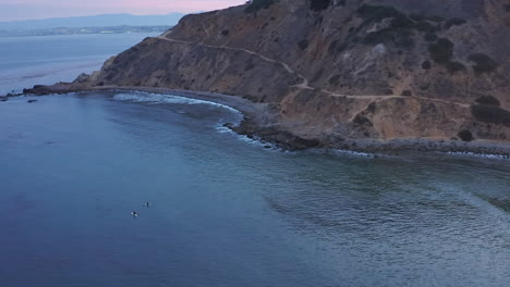 Surfers-sit-on-their-longboards-and-wait-for-the-perfect-wave-at-sunset---aerial-view-of-Rancho-Palos-Verdes-bluff-and-beach