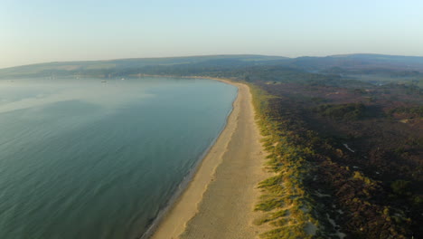 An-aerial-shot-flying-along-the-sandy-British-beach-of-Studland-Bay-on-the-Dorset-coast-at-sunrise-with-beautiful-light-in-the-summer