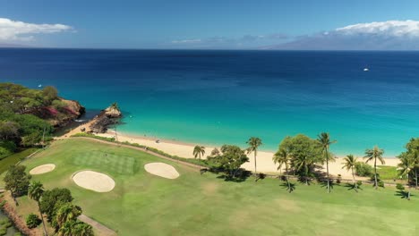 Slow-aerial-spinning-view-of-white-birds-over-a-golf-course-and-beach-in-maui,-Hawaii