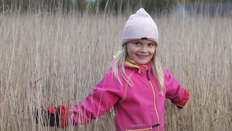 Smiling-little-blond-girl-playing-on-meadow-on-winter-day-and-looking-in-camera