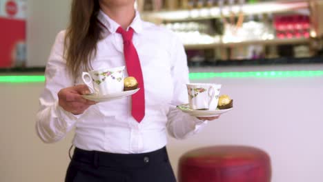 Elegant-Gekleidete-Kellnerin-Serviert-Gästen-Eine-Tasse-Kaffee-Und-Eine-Bar-Im-Hintergrund-Im-Musikinstrumenten-Restaurant-In-Zeitlupe