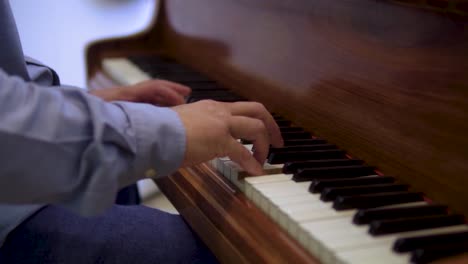 caucasian-male-in-smart-casual-clothing-plating-wooden-vintage-piano-hands-close-up-blurred-backround-slow-motion