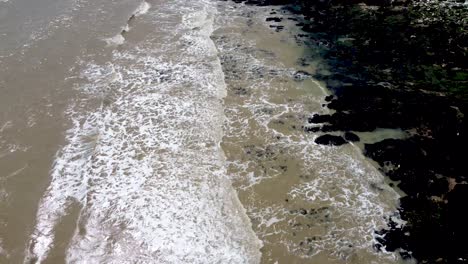 4K-drone-video-of-waves-coming-to-shore-over-rocks-with-seaweed-and-sand