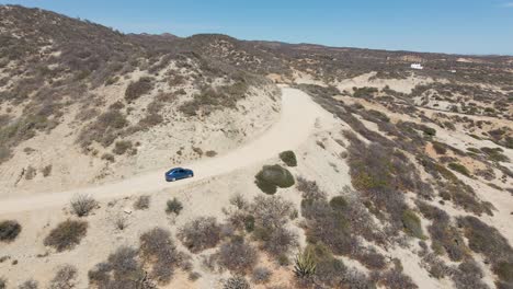 Aerial:-car-driving-on-mountain-dirt-road-through-desert,-4K-drone-tracking-view