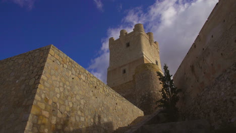 Low-angle-view-of-The-Atalaya-Castle-where-clouds-are-moving-under-the-blue-sky,-Villena,-Province-of-Alicante,-southern-Spain