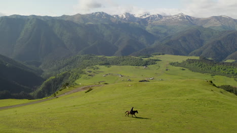 Wide-cinematic-paning-drone-shot-of-man-riding-a-horse-in-upper-Omalo,-Tusheti-Georgia