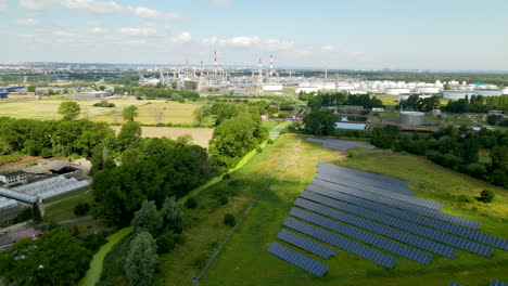 Eco-friendly-solar-panel-farm-on-grass-field-and-Eco-unfriendly-industrial-factory-in-background