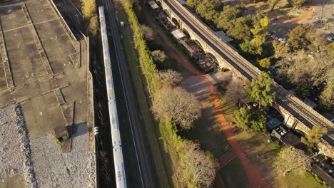 Impressive-aerial-view-of-a-modern-train-moving-along-the-tracks-in-the-middle-of-an-urban-area-at-sunset