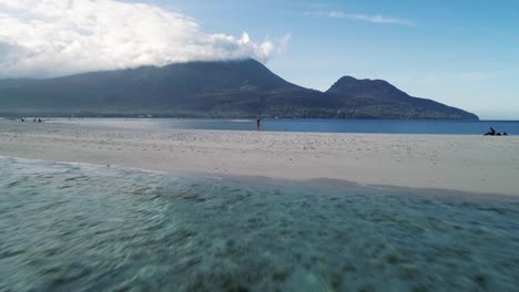 Flying-past-pretty-blond-woman-standing-alone-on-white-island-beach,-Camiguin