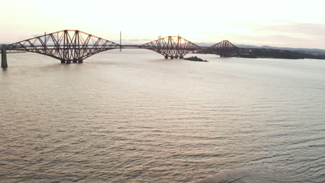 A-drone-shot-panning-up-to-reveal-the-Forth-Rail-Bridge,-in-Queensferry,-Scotland,-UK-filmed-at-sunset