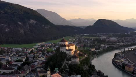 Aerial-footage-of-mountain-town-Kufstein-with-hilltop-fortress,-summer-scenery-at-sunrise,-river-Inn-meandering-through-the-valley---Austrian-Alps-from-above,-Tyrol,-Austria,-Europe