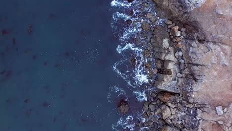 Waves-breaking-against-the-rocky-shore-near-Rancho-Palos-Verdes-in-Southern-California---straight-down-aerial-view