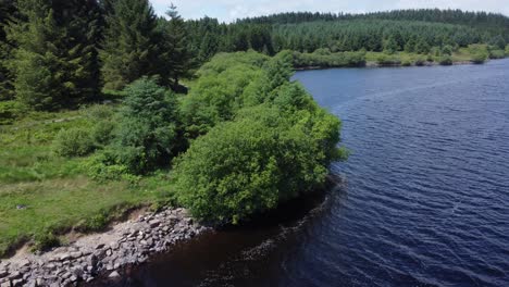 Idyllic-blue-water-reservoir-lake-woodland-hiking-walk-aerial-view-orbit-low-right-over-loch