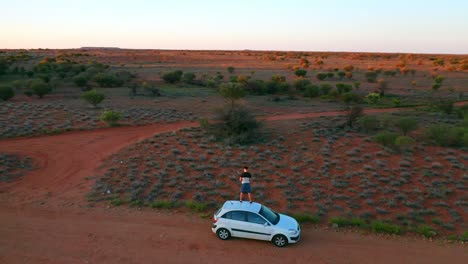 Umlaufende-Luftaufnahme-Eines-Mannes,-Der-Auf-Einem-Auto-Mitten-Im-Australischen-Outback-Steht---Northern-Territory-Australien