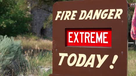 EXTREME-Fire-Danger-Today-red-and-white-sign-on-brown-metal-board-wide-shot-that-whips-straight-up-to-view-mountains-at-national-park-during-wildfire-crisis-in-the-US-and-world