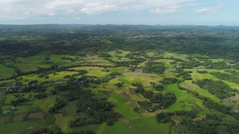 Green-countryside-of-Bohol-with-distant-Chocolate-mountains,-Philippines,-aerial
