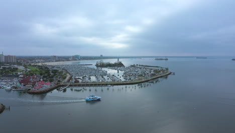 A-yacht-leaves-the-Long-Beach,-California-harbor-for-the-open-waters-of-the-Pacific-Ocean-on-an-overcast-morning---aerial-view-in-slow-motion