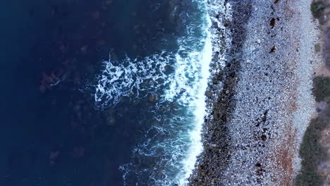 Waves-crashing-against-a-picturesque-rocky-shoreline---tilt-up-aerial-reveal