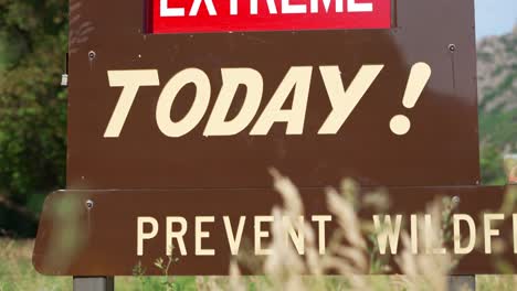 EXTREME-Fire-Danger-Today-Prevent-Wildfire-red-and-white-sign-on-brown-metal-board-wide-shot-panning-down-and-to-the-right-at-national-park-mountains-Ogden-Utah-Canyon