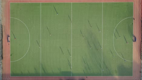 Aerial-top-down-time-lapse-of-hockey-player-playing-game-in-green-hockey-court-during-sunset