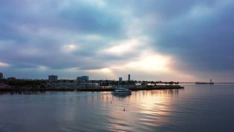Eine-Luxusyacht-Segelt-Bei-Sonnenaufgang-Durch-Den-Hafen-Von-Long-Beach,-Kalifornien,-Wobei-Der-Sonnenaufgang-Vom-Glasigen-Wasser-Reflektiert-Wird