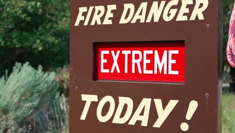 Extreme-Brandgefahr-Heute-Rotes-Und-Weißes-Schild-Auf-Braunem-Metallbrett-Mit-Sträuchern,-Büschen-Und-Bäumen-Im-Wind-Im-Hintergrund-Weitschuss-Im-Nationalpark-In-Ogden,-Utah