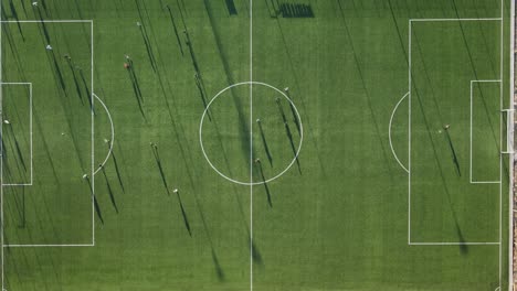 Aerial-top-down-timelapse-of-young-players-playing-soccer-football-game-on-court-of-university-during-sunny-day