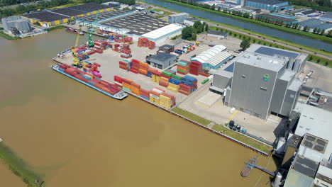 Flying-towards-small-shipyard-with-a-docked-cargo-boat-loaded-with-containers