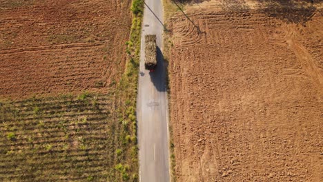 Luftaufnahmen-Eines-Mit-Zuckerrohr-Beladenen-Lastwagens,-Der-Am-Nachmittag-Durch-Ackerland-Auf-Einer-Schmalen-Asphaltstraße-In-Thailand-Fährt