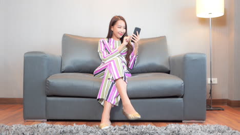 A-young-pretty-woman-sitting-on-a-sofa-taps-text-messages-into-her-smartphone