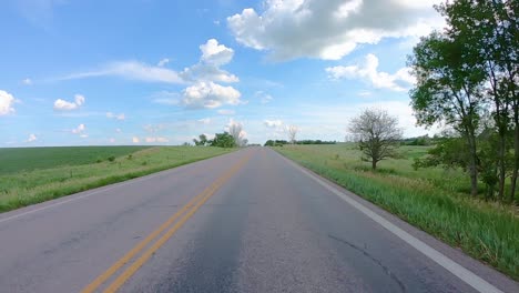 POV-while-slowly-driving-down-a-country-road-in-South-Dakota,-past-luscious-green-fields-of-corn-and-a-few-trees