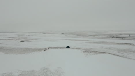 Slow-orbiting-aerial-of-UTV-side-by-side-in-middle-of-barren-snowy-prairie,-4K
