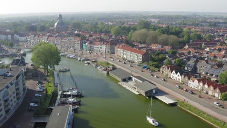 Aerial-shot-of-a-sailboat-sailing-on-a-waterway-through-the-historical-town-of-Middelburg,-the-Netherlands,-on-a-sunny-summer-evening