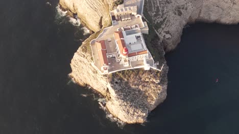 Tilt-up-aerial-view-of-Cabo-de-Sao-Vicente-lighthouse-overlooking-the-ocean,-Sagres,-Algarve