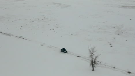 Wide-aerial-tracking-UTV-side-by-side-driving-through-snowy-field-winter,-4K