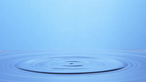 Slow-motion-shot,-two-drops-of-water-falling-on-light-blue-surface-creating-a-water-pillar