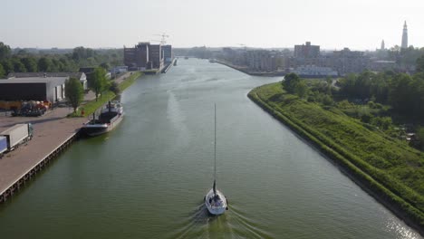 Aerial-shot-of-a-sailboat-sailing-on-the-Canal-through-Walcheren-towards-the-historical-town-of-Middelburg-in-Zeeland,-the-Netherlands,-on-a-warm,-sunny-summer-evening