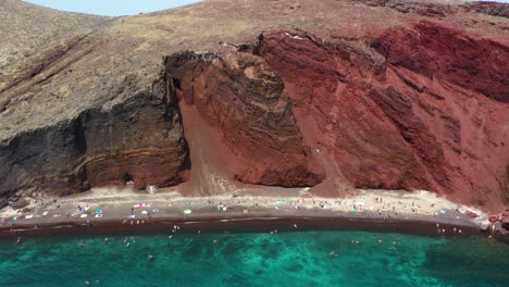 Aerial-top-down-revealing-Red-Beach-with-turquoise-water,-mountains-and-red-colored-sand-in-Santorini,-Greece
