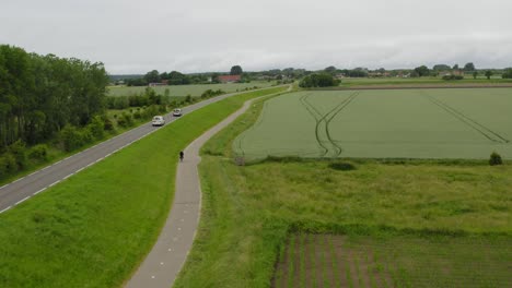 Long-aerial-tracking-shot-of-traffic-through-agricultural-land-on-the-peninsula-of-Walcheren-in-Zeeland,-the-Netherlands,-on-a-cloudy-summer-day