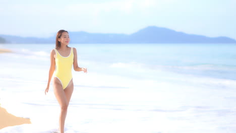 A-healthy,-fit,-attractive-young-woman,-in-a-one-piece-yellow-bathing-suit,-walks-through-the-incoming-surf