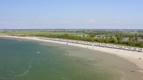 Aerial-backward-establishing-shot-of-a-group-of-kitesurfers-practicing-by-the-beach-on-a-windy-day-near-Wissenkerke,-the-Netherlands