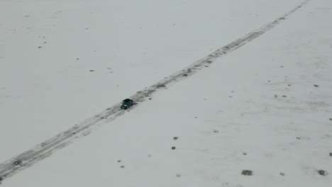 Aerial-shot-looking-down-as-UTV-side-by-side-drives-down-snow-covered-road,-4K