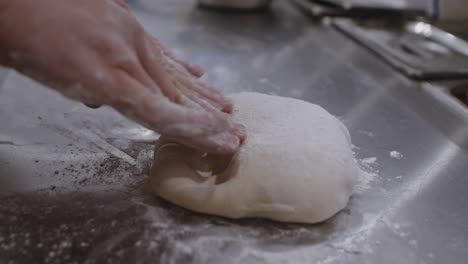 Forming-by-hand-neapolitan-pizza-ball-dough-into-the-circle-on-cooking-table-in-pizzeria