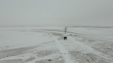 Aerial-following-shot-UTV-side-by-side-driving-across-snowy-field,-4K