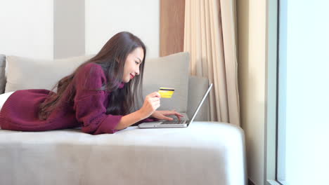 Compras-En-Línea-Desde-El-Sofá,-Joven-Mujer-Asiática-Feliz-Comprando-Cosas-En-Internet-Usando-Tarjeta-De-Crédito-Y-Computadora-Portátil,-Fotograma-Completo