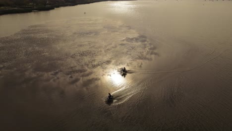 Slow-motion-aerial-shot-of-two-motorcycles-driving-over-water-surface-at-sunset-after-strong-rain
