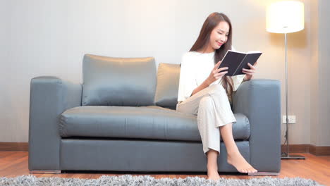 A-young-woman-sits-on-a-couch-under-a-floor-lamp-reads-a-book