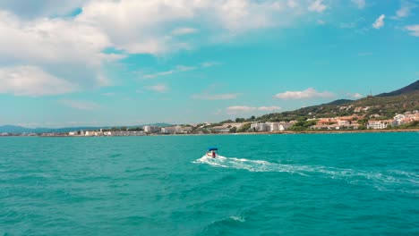 POV-boat-ride-following-small-speed-boat-on-beautiful-blue-sea-alongside-coastline-in-Spain,-Europe